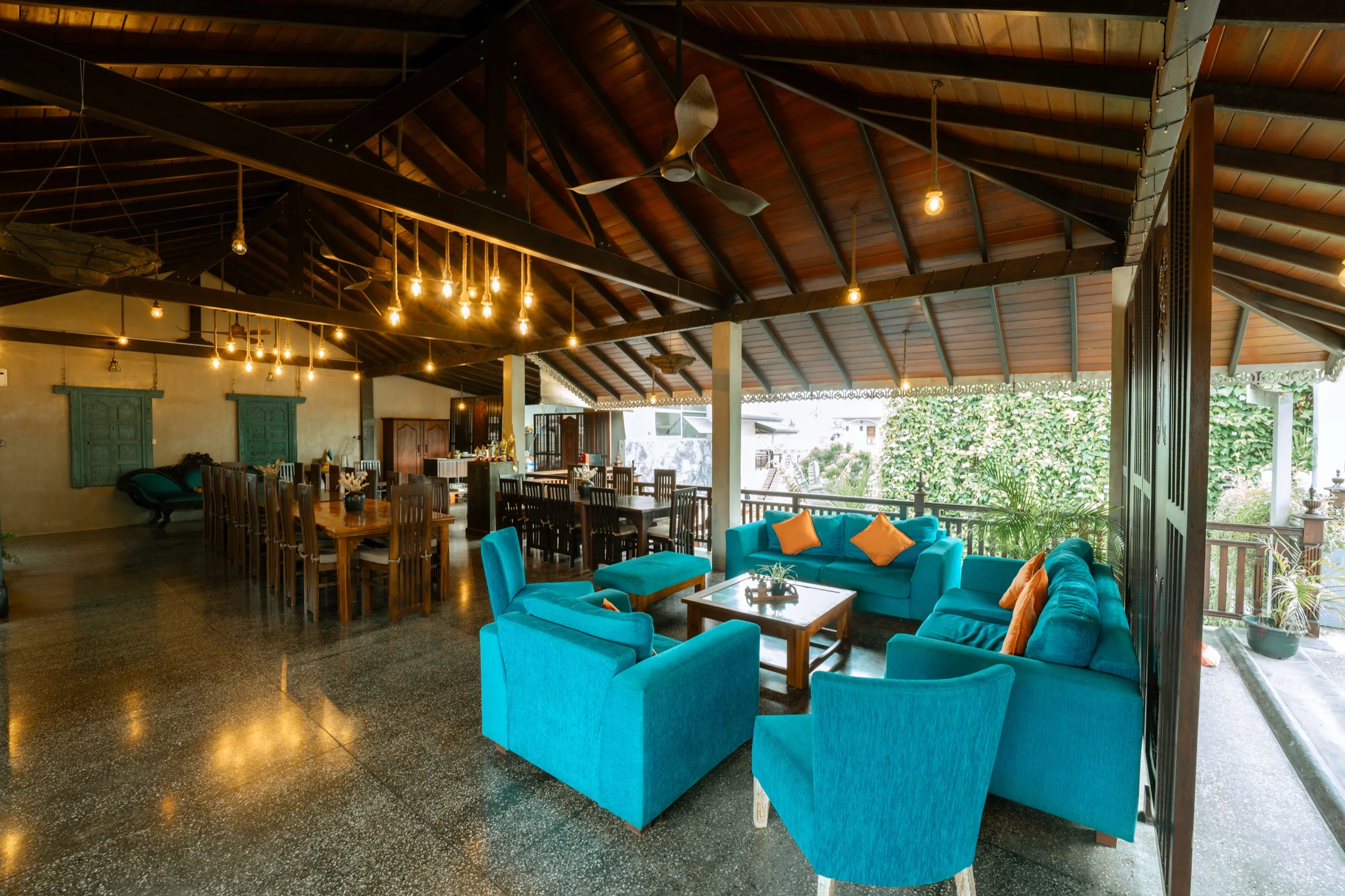 The villa's third floor: turquoise sofas, a long timber dining table and hanging filament bulbs under the dark roof